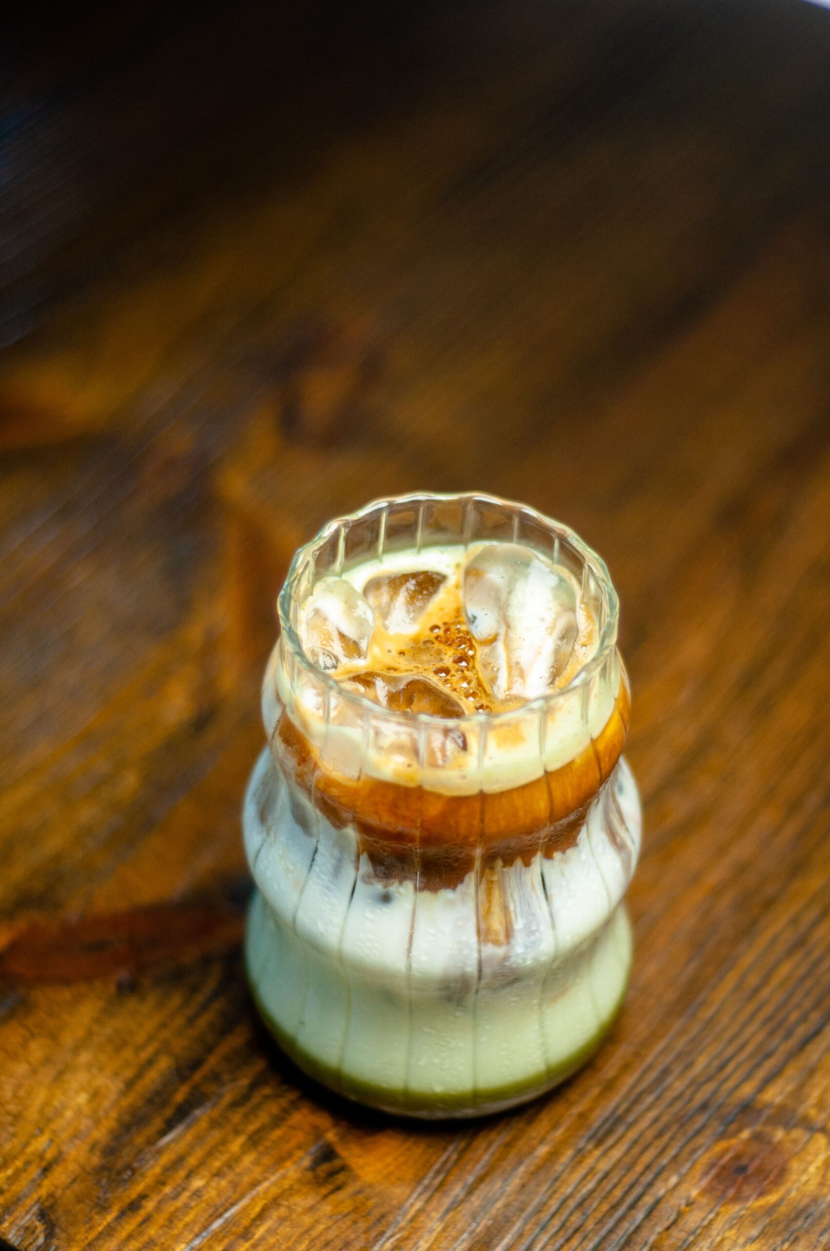 Eine Detailaufnahme eines geschichteten Eiskaffees in einem geriffelten Glas auf einem Holztisch.