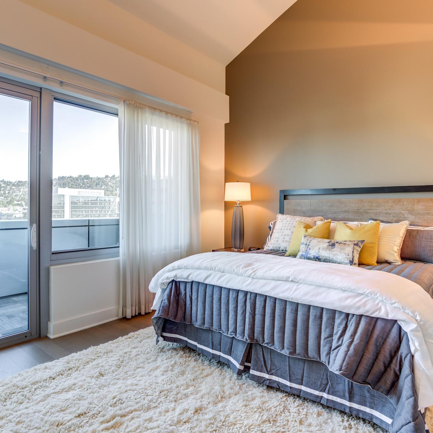 Studio Apartments in Berkeley, CA - Spacious Bedroom with Large Window, Wood Flooring, and Accent Wall.